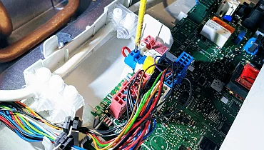 A boiler circuit board with wiring and coloured electrical connectors visible.